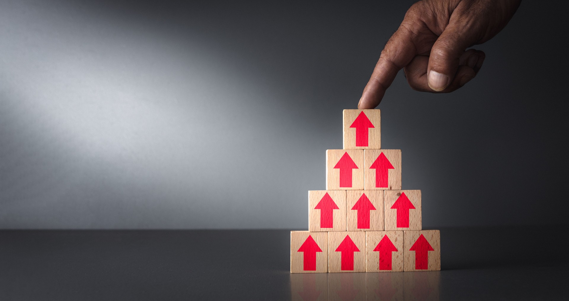 concept of mounting inflation and the cost of living . arrows pointing up on wooden blocks with hand on grey blue background .